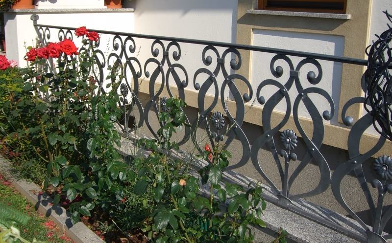 Balkongeländer mit großen Eisenvoluten und Blumenkasten
